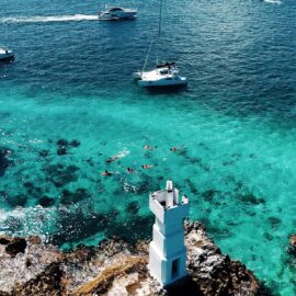 Catamaran cercano a arrecife y un faro