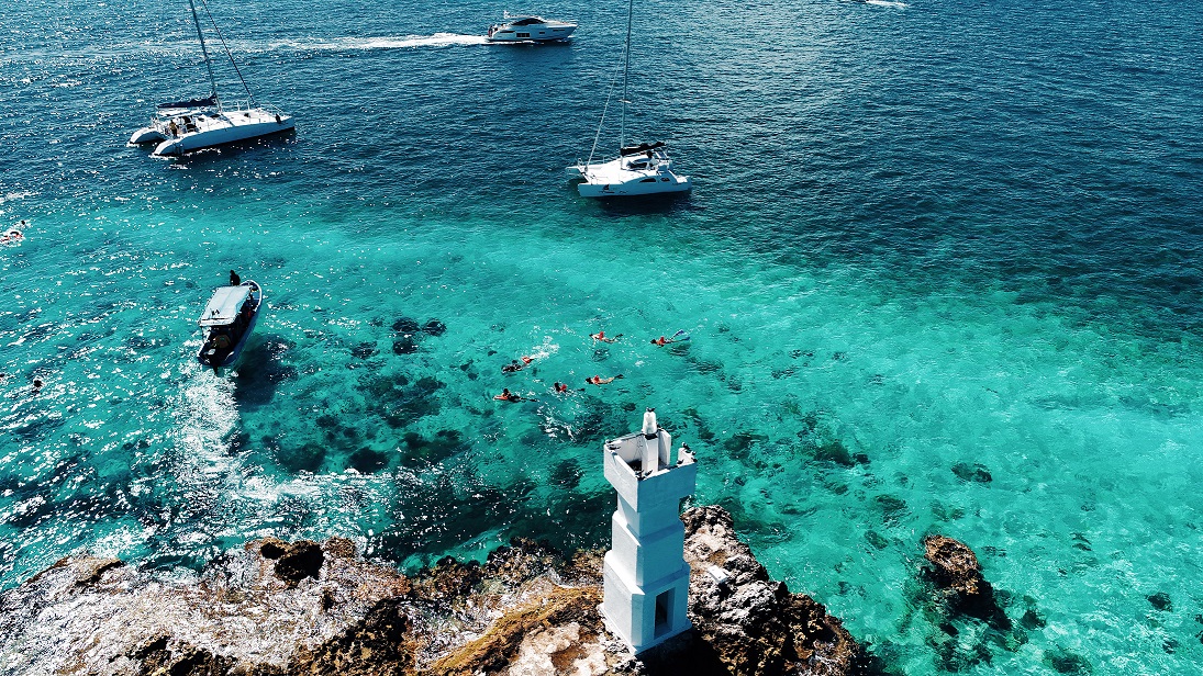 Catamaran cercano a arrecife y un faro